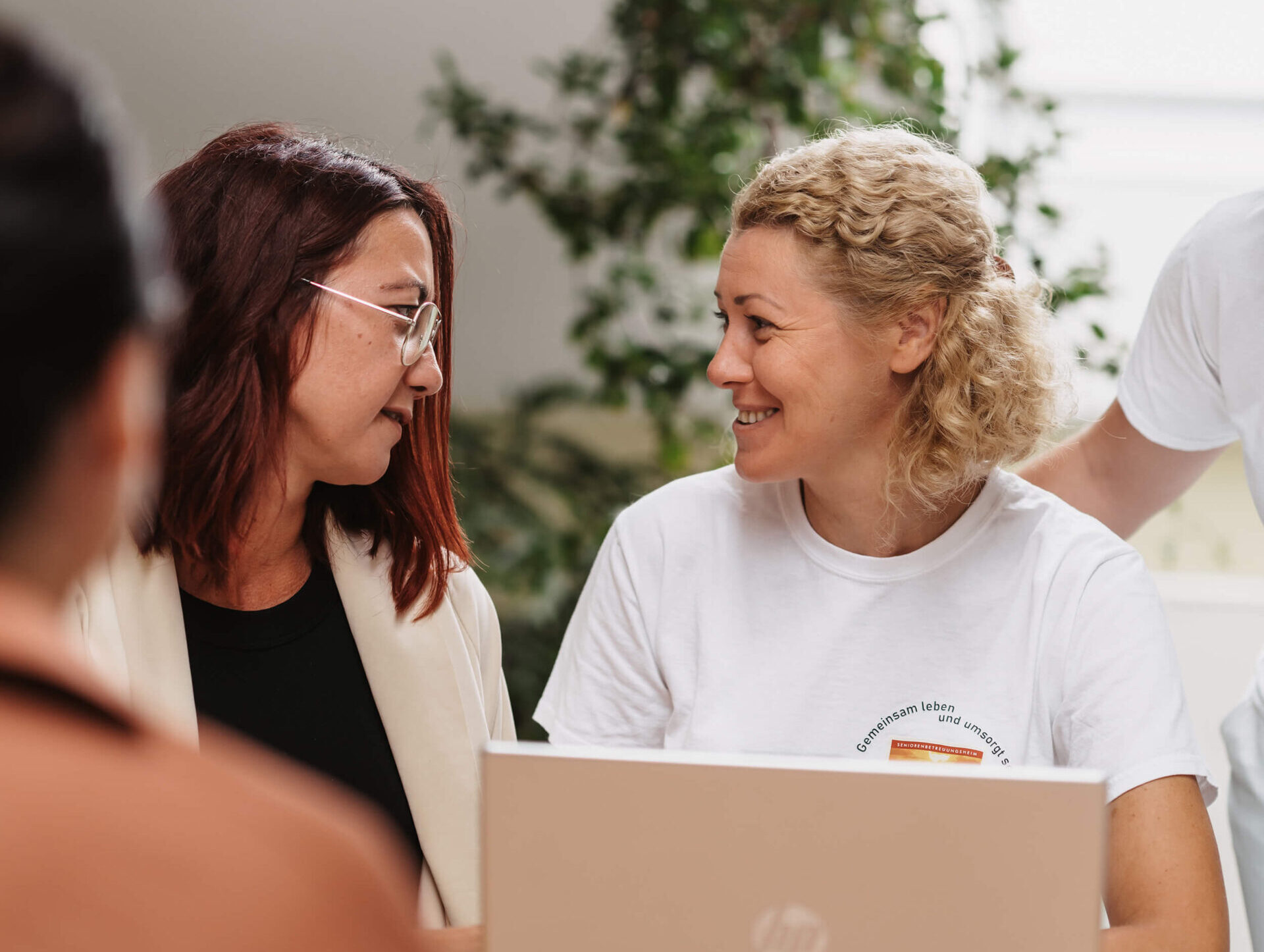 Zwei Frauen lächeln sich bei einem Gespräch am Laptop an