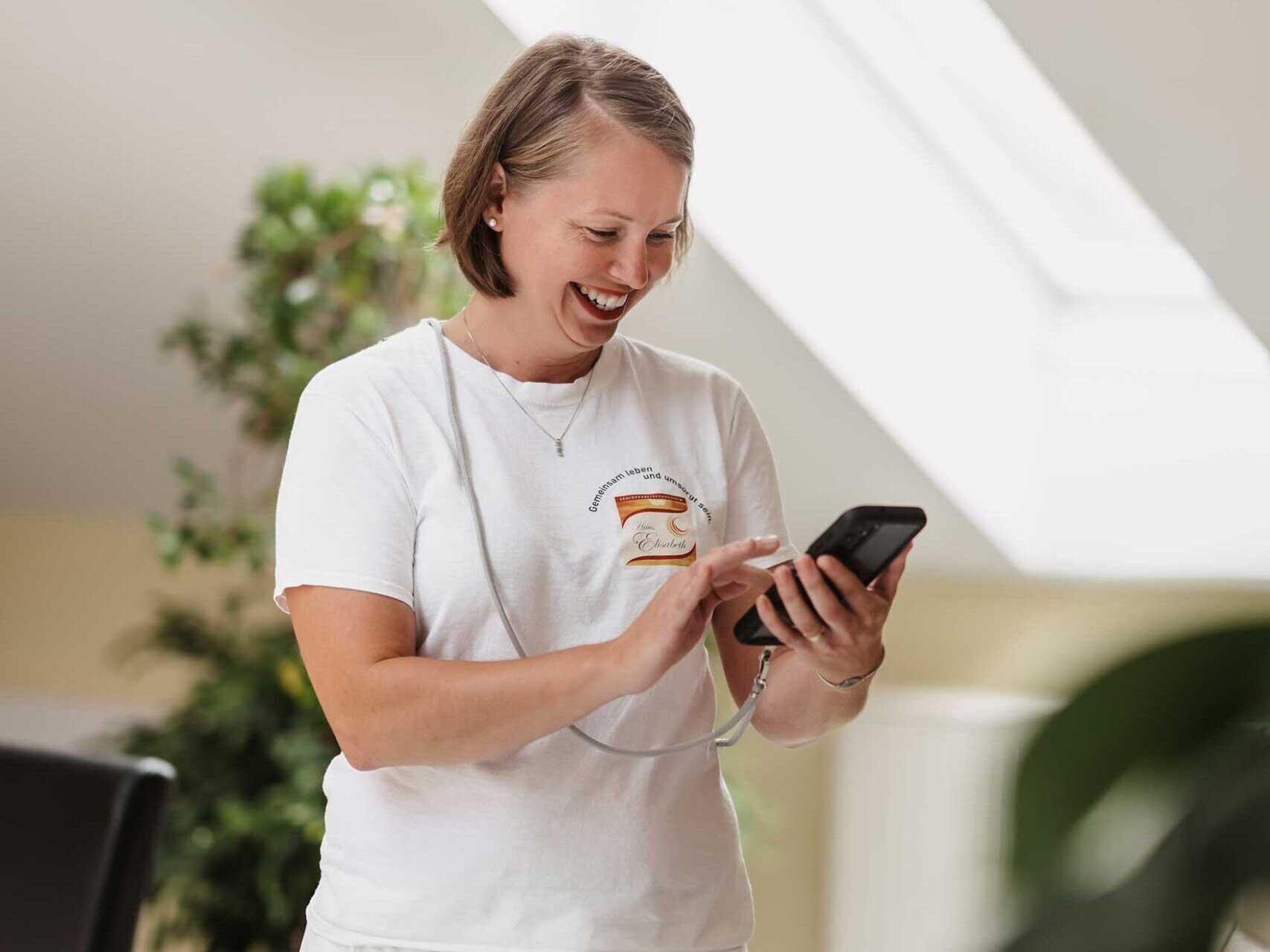 Pflegekraft lächelt und bedient ein Smartphone zur Dokumentation
